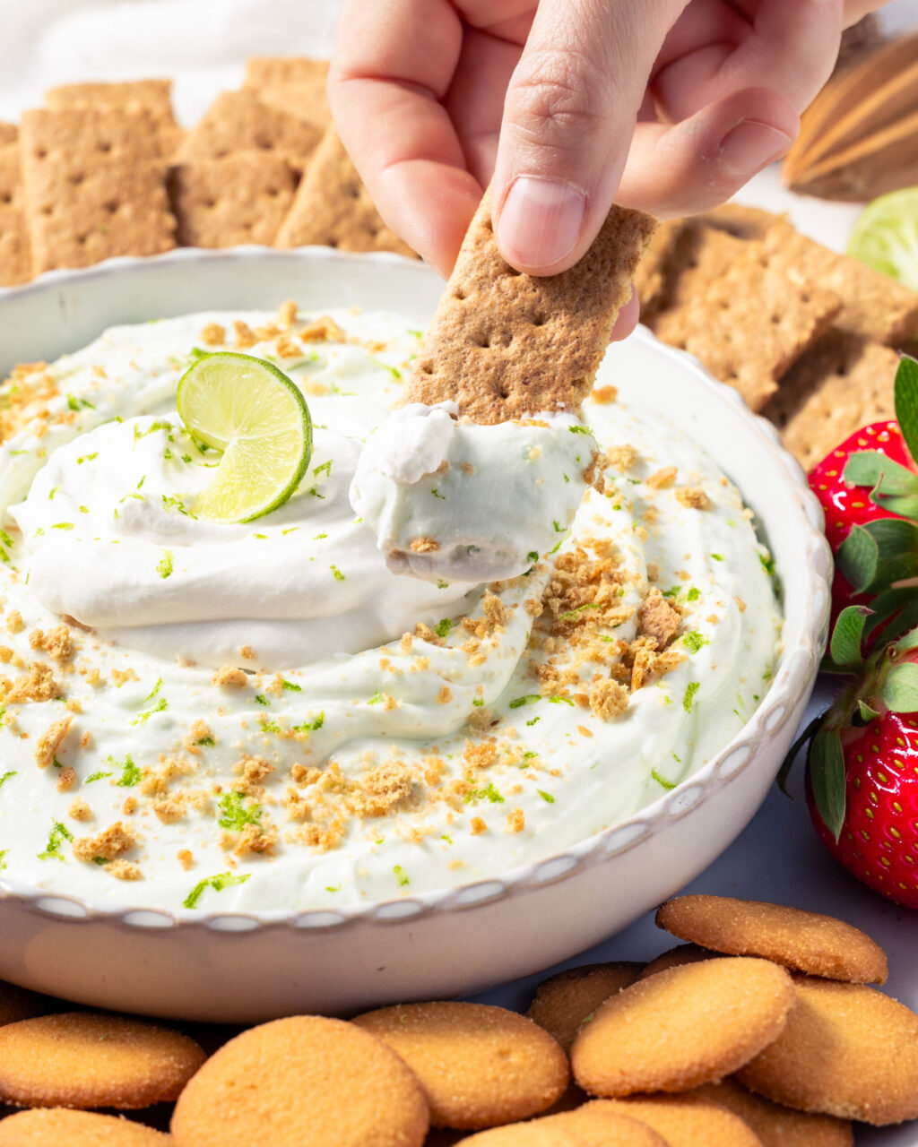 Key Lime Pie Protein Cheesecake Dip topped with whipped cream and served with graham crackers, Nilla wafers, and strawberries