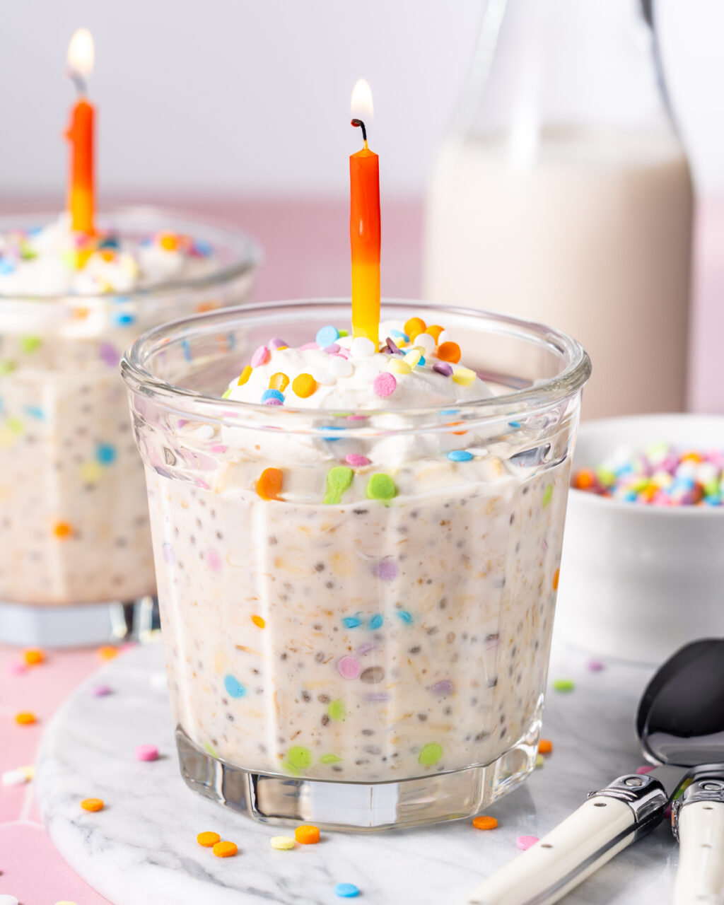 Birthday cake protein overnight oats in a glass jar with whipped cream and sprinkles on top and a lit birthday cake candle