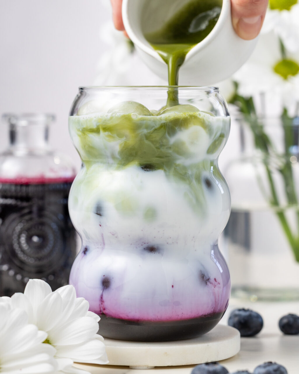 Blueberry Matcha Iced Latte with matcha tea being poured into the glass over ice and blueberry syrup.